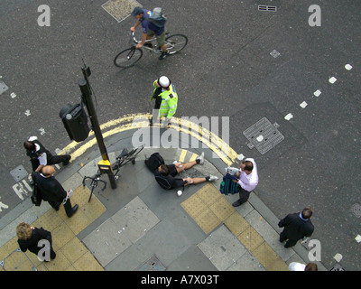 Vista aerea del ciclista steso sul marciapiede che riceve cure con l'agente di polizia e testimone dopo l'incidente sulla City of London Street Foto Stock