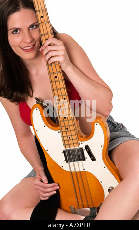 Giovane donna che sorride mentre tiene una chitarra basso tra le gambe in un ritratto di studio creativo, USA. Foto Stock