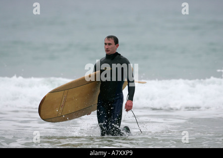 Surfista maschio con la scheda madre viene fornita al di fuori del mare in piena muta in acqua su tra Na spiaggia Rossan fuori Downings County Donegal Foto Stock