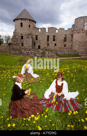 Tre donne vestiti in abiti tradizionali il prelievo di tarassaco davanti a un castello a Cesis, Lettonia. Foto Stock