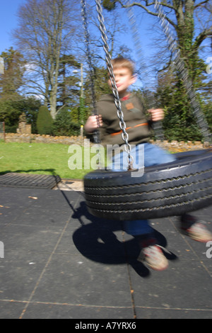 Ragazzo giocando sul parco giochi tire swing sfocatura del movimento Foto Stock