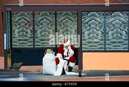 Babbo Natale legge il suo naughty e bella lista in attesa per un autobus Foto Stock