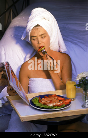 La donna in bianco asciugamani da bagno di mangiare la frutta sana colazione e rivista di lettura Foto Stock