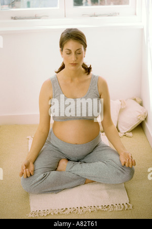 Fortemente incinta Donna eseguendo lo yoga per il rilassamento in ambienti interni Foto Stock