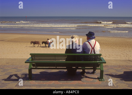 Vecchia coppia seduta sul banco di lavoro guardando fuori verso la spiaggia e la passeggiata lungomare a Mablethorpe nel Lincolnshire England Regno Unito Foto Stock