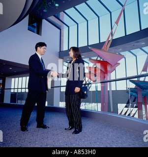 Asian l uomo e la donna in piedi sulla piscina piano mezzanino del moderno edificio commerciale. Il messaggio di saluto di handshake. Foto Stock