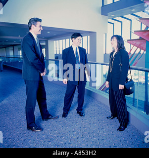 Due uomini e una donna in abiti aziendali in piedi sul mezzanino all'interno dell'edificio. Foto Stock