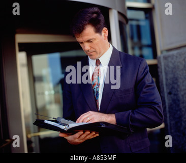 Business Professional. Executive l uomo al di fuori della città edificio per uffici. Guardando nel diario. Foto Stock