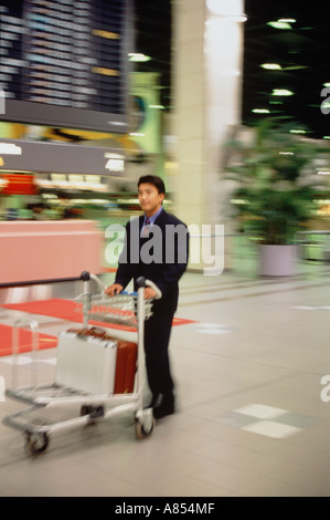 Giovane imprenditore spingendo carrello bagagli in aeroporto terminal. Foto Stock