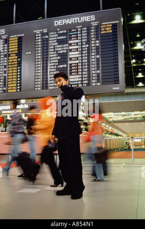 Giovane uomo che indossa una tuta di business, utilizzando un telefono mobile all'interno di terminal di un aeroporto. Foto Stock