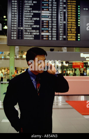 Giovane uomo che indossa una tuta di business, utilizzando un telefono mobile all'interno di terminal di un aeroporto. Foto Stock