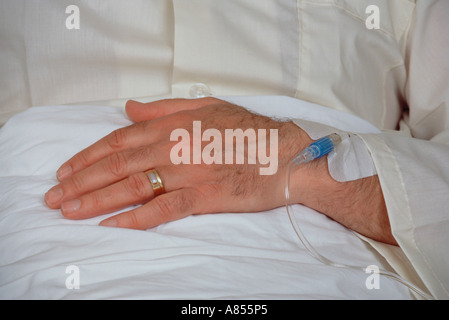 Close-up pf mano di mezza età uomo nel letto di ospedale con la somministrazione endovenosa di fleboclisi saline collegata. Foto Stock
