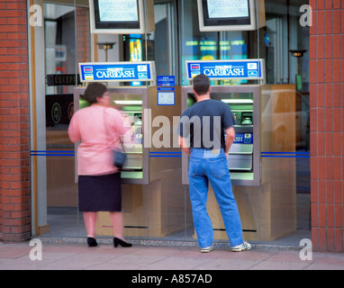 Le persone che usano le macchine di contanti presso una filiale della Banca Halifax plc, Inghilterra, Regno Unito. Foto Stock