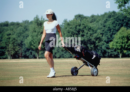 Donna giocatore di golf sul green tirando carrello da golf Foto Stock