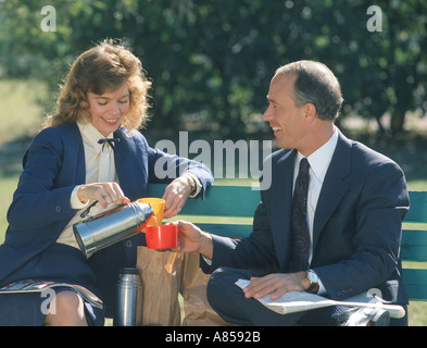 Azienda giovane godendo il pranzo su una panchina nel parco a mezzogiorno Foto Stock