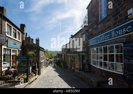 Negozi e caffetterie sulla strada principale nel centro del villaggio, Haworth, West Yorkshire, Inghilterra, Regno Unito Foto Stock