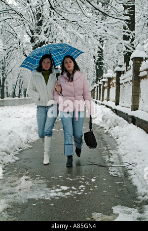 Due giovani caucasici donna camminando lungo una città europea marciapiede durante l'inverno la neve Foto Stock