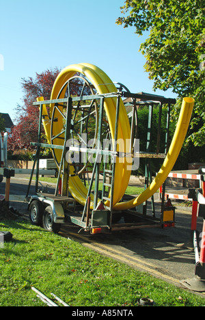 Gas principale posa di tubi lavori stradali in corso con grande bobina di tubo di plastica flessibile giallo sul rimorchio Essex Inghilterra UK con spazio di copia Foto Stock