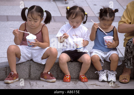 Le tre ragazze seduto su un cordolo di metà estate godendo di un fresco kakigori o radere ghiaccio, trattare Foto Stock