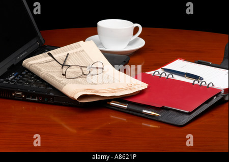 Ambiente di ufficio con tazza di caffè, laptop, giornale, bicchieri, penne e appuntamento del calendario Foto Stock