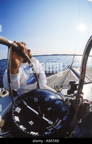 Man at helm of sailboat with hand on wheel and showing compass heading Foto Stock