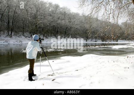Inverno di osservazione degli uccelli femmina utilizzando cannocchiale lungo il fiume nevoso Bank Foto Stock