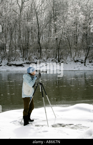 Inverno di osservazione degli uccelli femmina utilizzando cannocchiale lungo il fiume nevoso Bank - Verticale Foto Stock