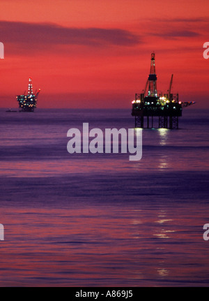 Pozzi petroliferi offshore contro la luce del tramonto a Huntington Beach, California Foto Stock