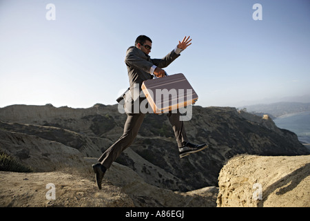 Business man saltando su una scogliera valigetta di contenimento. Foto Stock