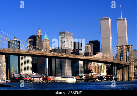 Il ponte di Brooklyn attraversa l'East River con lo skyline di Lower Manhattan e le iconiche torri gemelle del World Trade Center visibili sotto un cielo azzurro Foto Stock