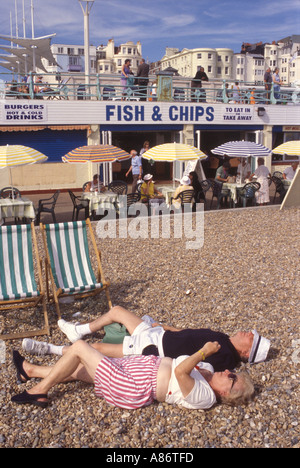 Coppia anziana in pensione sdraiata sulla spiaggia di ciottoli che prendeva il sole rilassata durante le vacanze Brighton East Sussex, Inghilterra anni '2001 2000 UK HOMER SYKES Foto Stock