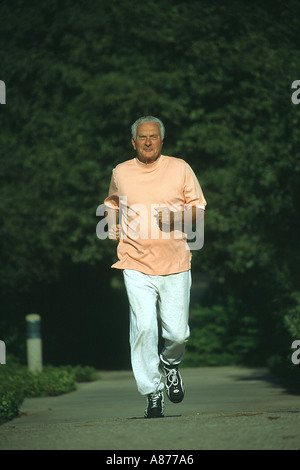 Un sorridente senior citizen maschio 70s 73 anni anni di indossare pantaloni di sudore orange t shirt jogging giù un percorso in un parco Caucasian POV SIGNOR ©Myrleen Pearson Foto Stock