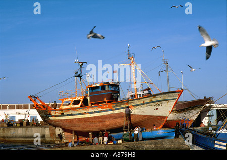 Lavoratori che riparano e rivernicono barche da pesca in darsena nel porto di Essaouira, Marocco Foto Stock