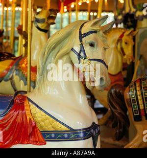 Chiudere fino a un bianco Merry Go Round cavallo accanto ad altri cavalli in legno su pali in ottone Foto Stock