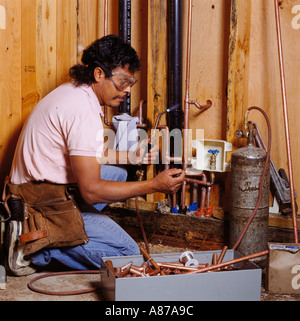 Un Latino idraulico utilizza una torcia di acetilene per saldare insieme i tubi di rame per la costruzione di una casa Foto Stock