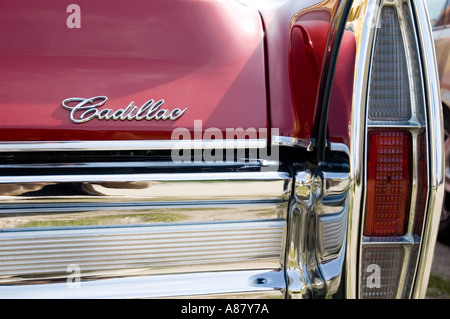 Primo piano dettagliato di una Cadillac rossa d'epoca con logo classico, paraurti cromato e iconico complessivo luce di posizione posteriore verticale. Foto Stock