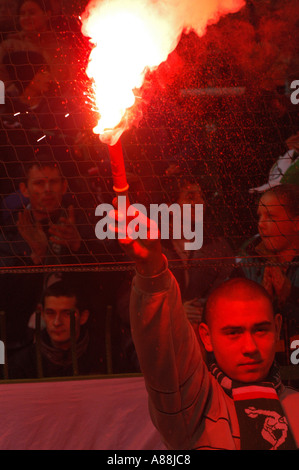 I tifosi di calcio che bruciano un bagliore rosso sulla terrazza di uno stadio di calcio, creando luce brillante e fumo durante una partita. Foto Stock