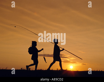 Silhouette di un giovane ragazzo e ragazza camminare a casa alla fine della giornata dopo che avevano passato la pesca Foto Stock