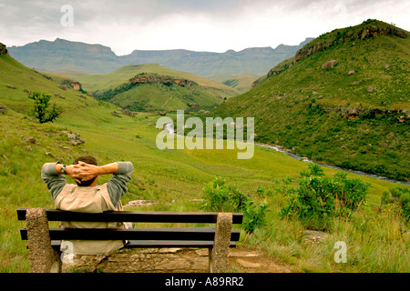 Un uomo su un banco di lavoro prende in vista alba del gigante del castello e le montagne Drakensberg nel Sud Africa Kwazulu Natal provincia. Foto Stock