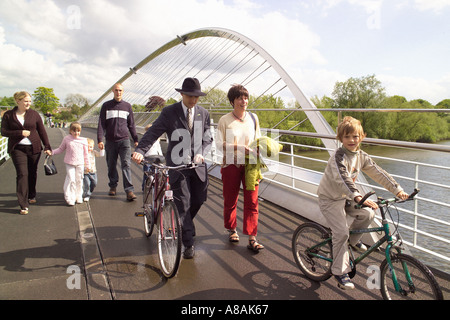 Pedoni e un giovane uomo vestito in modo intelligente che indossa una tuta intelligente e un cappello da trilby, spingendo una bicicletta sul Millennium Bridge. York. Foto Stock