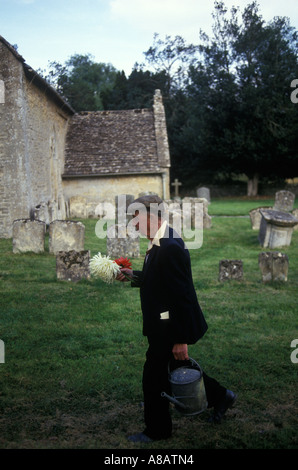 St Michael's e St Martin's Church Eastleach Turville uomo più anziano con fiori per la tomba della moglie. Trasporto di annaffiatoio. Gloucestershire 1990s Regno Unito 1993 Foto Stock