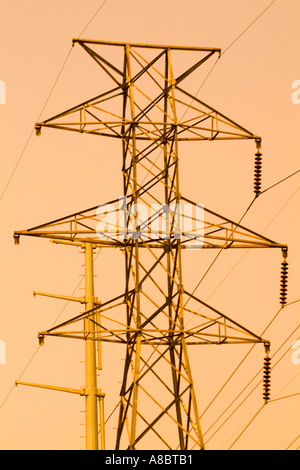 Tensione alta di alimentazione delle linee di trasmissione sulla trave torre contro il cielo arancione Foto Stock