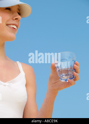 Ragazza sorridente indossando top bianco vetro di contenimento di acqua contro il cielo blu closeup copyspace Foto Stock