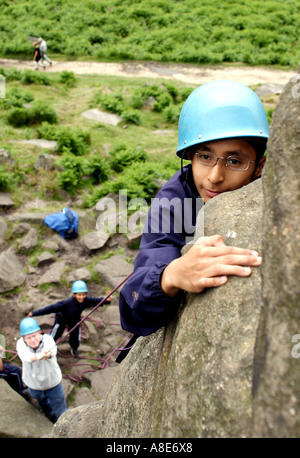 Un bambino disabile arrampicata su roccia durante una gita scolastica in Peak District Foto Stock