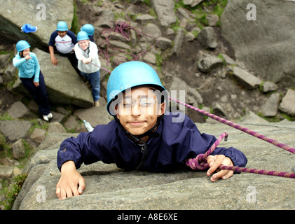 Un bambino disabile arrampicata su roccia durante una gita scolastica in Peak District Foto Stock