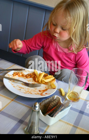 4 anno vecchia ragazza mangiando pesce e patatine in Seaside Cafe Foto Stock