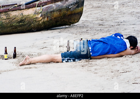 Un turista ubriaco passata fuori sulla spiaggia vicino a una canoa in Puerto Vallarta, Messico Foto Stock