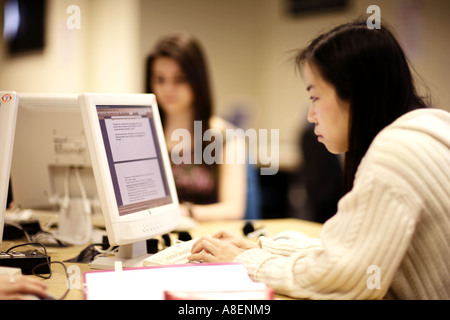 Feamle giovane studente cinese sta lavorando a un computer, una ragazza europea è a un altro PC in background ed è al di fuori della messa a fuoco Foto Stock