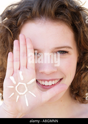 Giovane donna sorridente con la figura di un sole disegnato in crema solare sulla sua mano pelle giusta deve essere protetto contro la radiazione UV Foto Stock