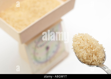 Ammucchiò cucchiaio di grana lunga riso essendo posto sulla bilancia da cucina per pesare Foto Stock